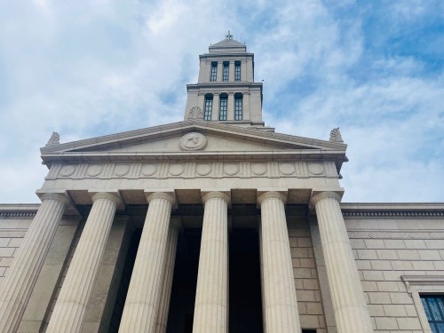 A grand building with tall columns and a clock tower under a cloudy sky.