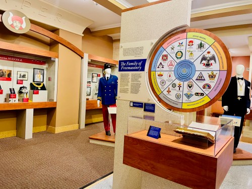 Exhibit showcasing Freemasonry artifacts, featuring a circular chart and display cases with historical items.