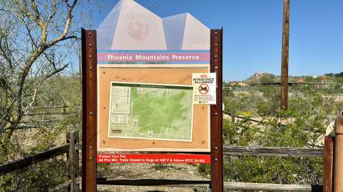 Sign at Phoenix Mountains Preserve displaying a trail map and pet policy information, surrounded by desert vegetation.