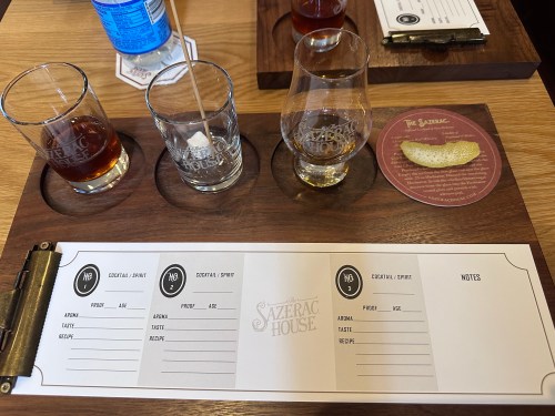 A wooden tasting board with three glasses, a tasting note sheet, and a lemon twist at Sazerac House.