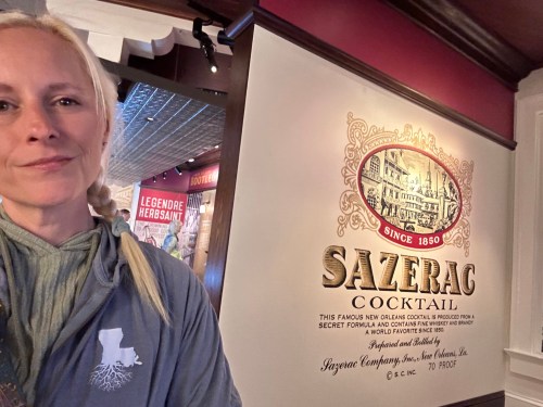 A person stands in front of a Sazerac cocktail sign, showcasing its history and significance in New Orleans.
