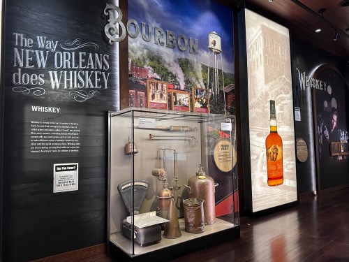 Exhibit showcasing New Orleans whiskey culture, featuring artifacts, a bourbon bottle, and informative displays.