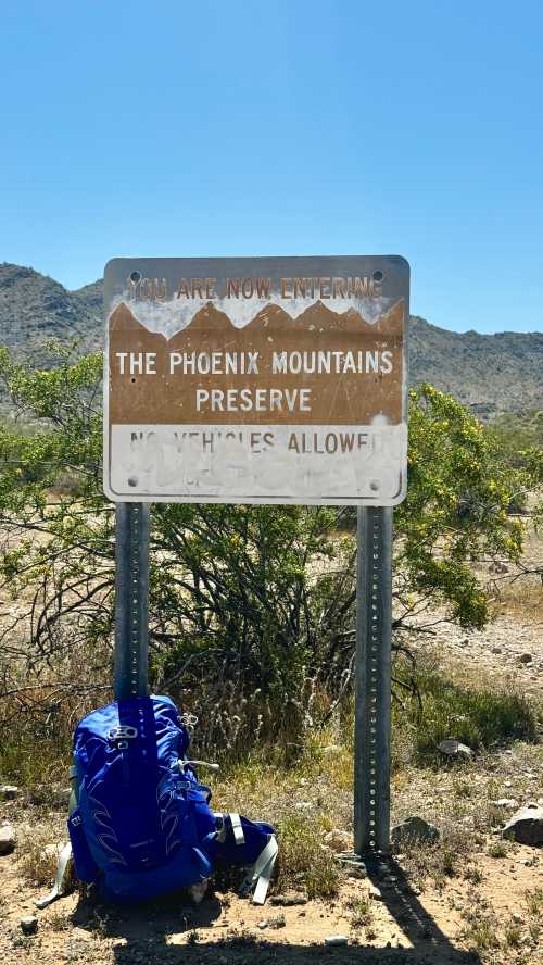 Sign marking the entrance to the Phoenix Mountains Preserve, with a blue backpack resting nearby.