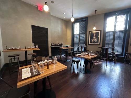 A modern dining room with wooden tables, chairs, and soft lighting, featuring a minimalist decor and large windows.
