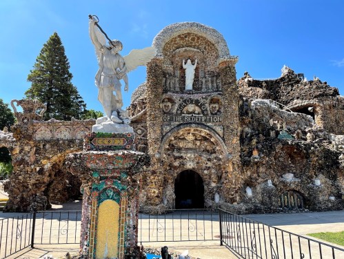 A stone structure with intricate designs, featuring a statue of an angel and a sign that reads "Holy Land of the Redemption."