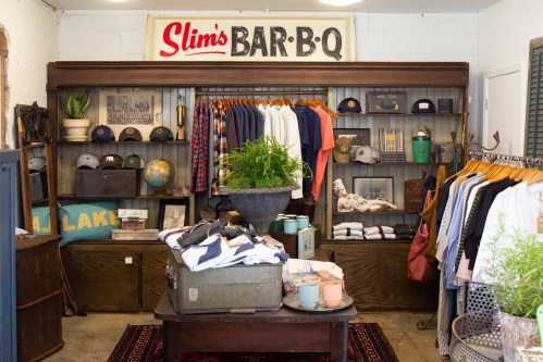 A cozy shop interior featuring clothing racks, vintage decor, and a sign for "Slim's Bar-B-Q" on the wall.