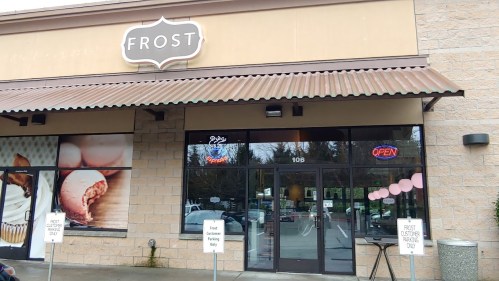 Exterior of a shop named "Frost," featuring an open sign and a decorative awning. Parking signs are visible in front.