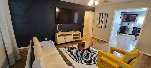 A modern living room with a beige sofa, yellow armchair, TV, and a coffee table on a striped rug.