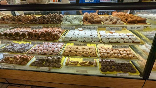 A display case filled with various types of donuts, including glazed, powdered, and cake varieties.
