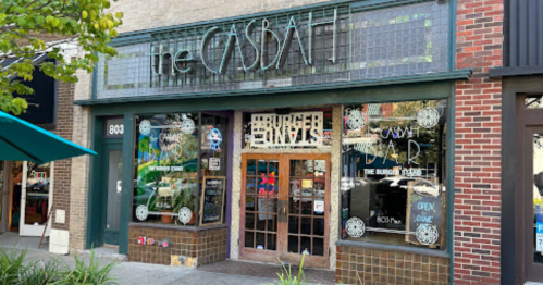Exterior of a restaurant called "The Casbah," featuring large windows and a colorful sign, with outdoor seating visible.