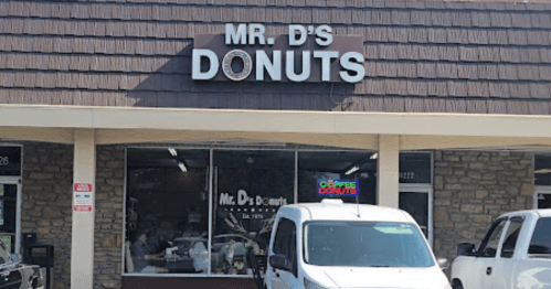 Exterior of Mr. D's Donuts shop, featuring a sign and large windows with customers inside. White van parked outside.