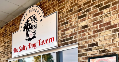 Sign for "The Salty Dog Tavern" on a brick wall, featuring a dog graphic and the phrase "Eat, Drink & Cheer."