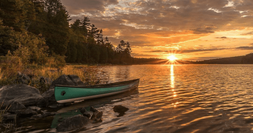 A serene lake at sunset with a canoe on the shore, surrounded by trees and reflecting golden light on the water.