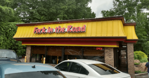 A restaurant named "Fork in the Road" with a yellow roof and an "OPEN" sign, surrounded by trees and parked cars.