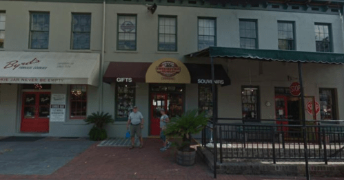 A street view of a building with shops, featuring a "Gifts" and "Souvenirs" sign, and people walking outside.