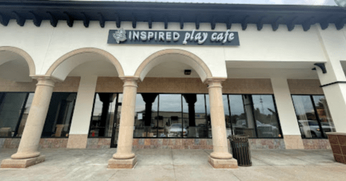 Exterior of a building with arched columns, featuring a sign that reads "Inspired Play Cafe."