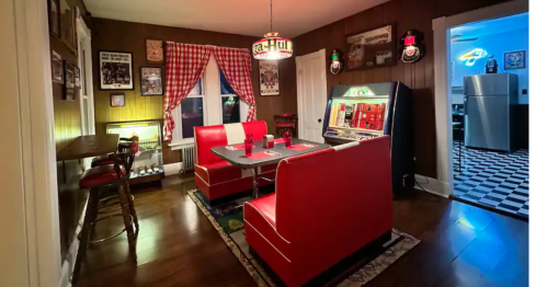 A retro diner-style dining area with red booths, a jukebox, and checkered flooring, illuminated by warm lighting.