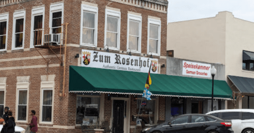 Exterior of Zum Rosenhof, an authentic German restaurant, featuring a green awning and nearby grocery store signage.
