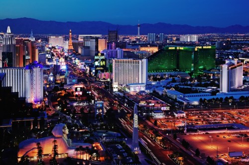 A vibrant night view of the Las Vegas Strip, featuring colorful lights, hotels, and the surrounding mountains.