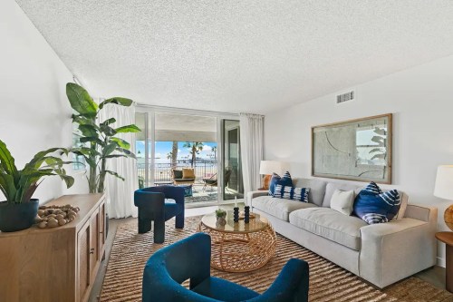 Bright living room with a sofa, blue chairs, a coffee table, and large windows showcasing a view of the outdoors.
