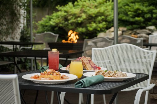A table set outdoors with colorful dishes, drinks, and a cozy fire in the background.