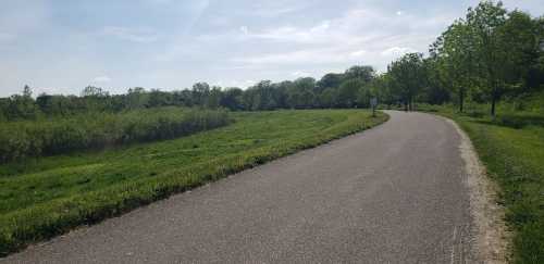 A paved path winds through a green landscape with trees and shrubs under a clear blue sky.