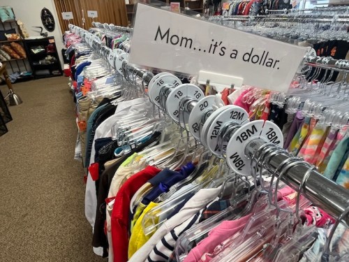 A clothing rack in a store with a sign saying, "Mom... it's a dollar," showcasing various children's clothes.