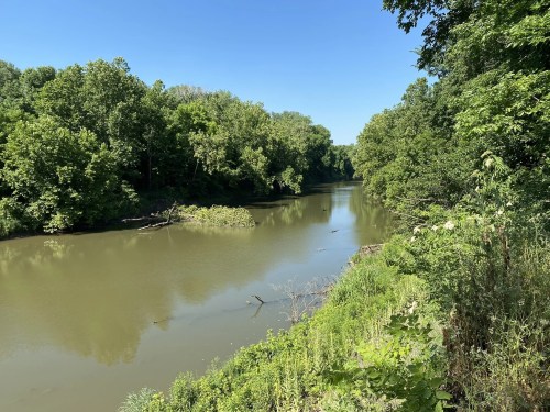 A serene river flows through a lush green landscape under a clear blue sky.