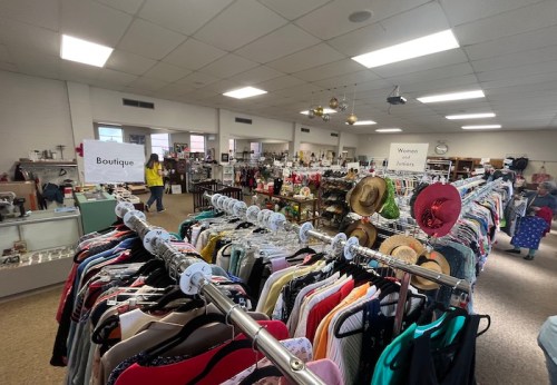 A spacious thrift store interior with racks of clothing, shelves of items, and signs for "Boutique" and "Women's Jeans."