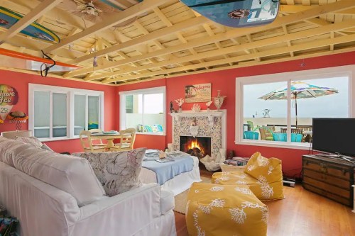Cozy beach-themed living room with a fireplace, colorful decor, and large windows overlooking a patio with umbrellas.