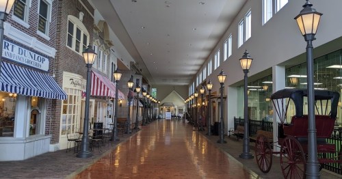 A spacious indoor shopping area with storefronts, decorative lamps, and a vintage carriage.