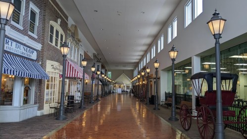 A spacious indoor shopping area with shops, street lamps, and a vintage carriage along a polished floor.