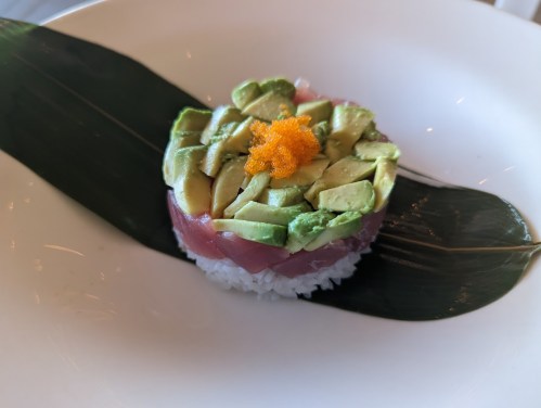 A sushi dish featuring rice topped with avocado, fish, and orange roe, served on a green leaf.