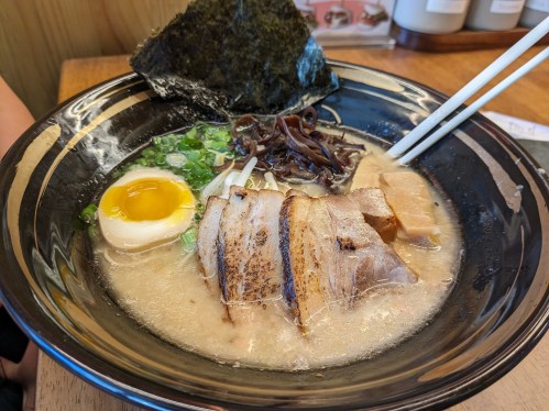 A bowl of ramen with sliced pork, a soft-boiled egg, seaweed, green onions, and mushrooms in a rich broth.