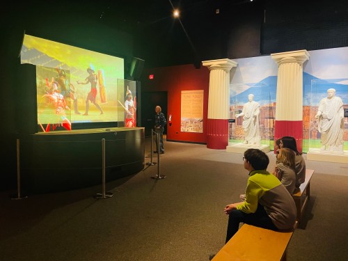 A group of visitors watches a vibrant display in a museum, featuring historical figures and scenes.