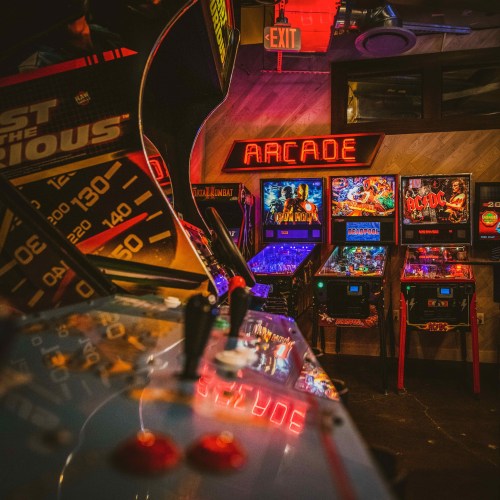 A vibrant arcade scene featuring pinball machines and classic arcade games, illuminated by colorful lights.