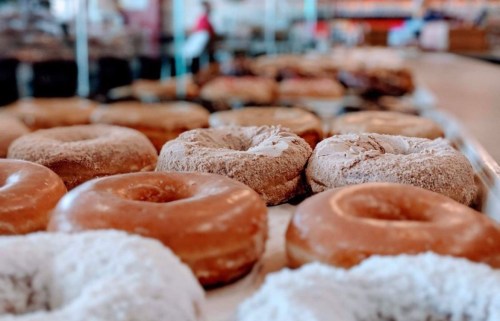 A variety of donuts on display, including glazed and powdered, in a bakery setting.