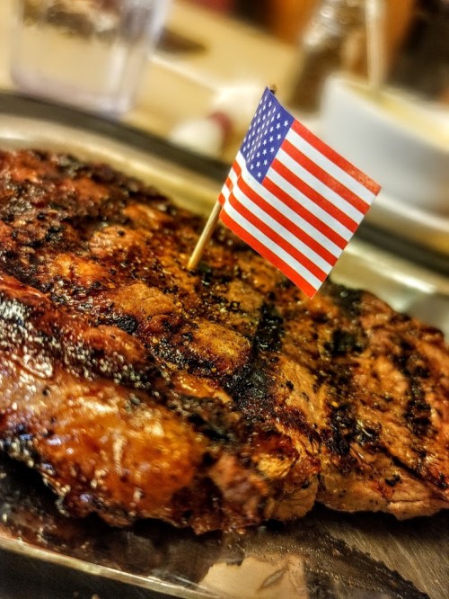 Grilled steak on a plate topped with a small American flag.
