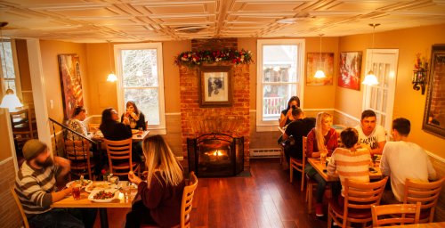 Cozy restaurant interior with diners at tables, a fireplace, and festive decorations on the walls.
