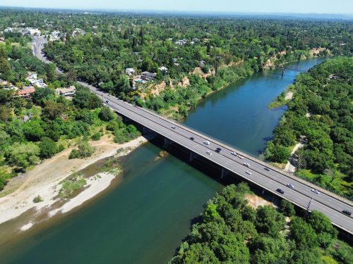 Aerial view of a bridge over a river, surrounded by lush greenery and a winding road.