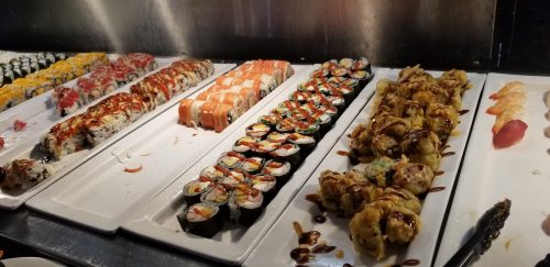 A variety of sushi rolls and sashimi displayed on white platters, featuring colorful toppings and sauces.
