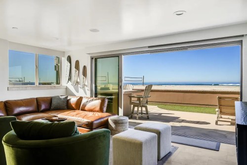 Cozy living room with a brown leather sofa, ocean view, and sliding glass doors leading to a patio.