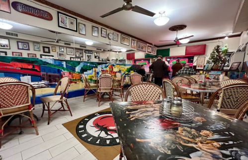 A cozy restaurant interior with colorful murals, wooden tables, and chairs, featuring framed photos on the walls.