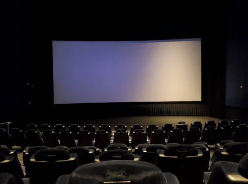 A darkened movie theater with empty seats facing a large, blank screen.