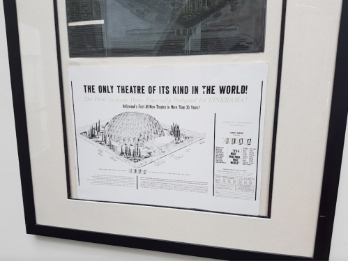 A framed vintage poster promoting a unique theater designed for Cinerama, featuring a dome structure and architectural details.