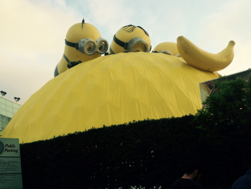 A large yellow structure resembling a banana, topped with cartoonish minion figures, set against a cloudy sky.