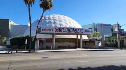Exterior of Pacific's Cinerama Theatre, featuring a large dome and boarded-up entrance, with palm trees in the foreground.