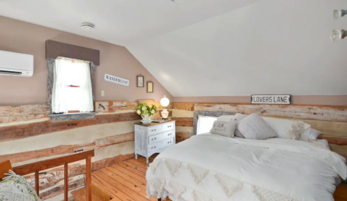 Cozy bedroom with a wooden bed, decorative signs, and a small nightstand, featuring rustic walls and soft lighting.
