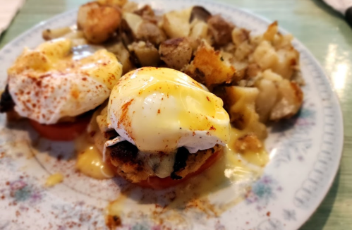 A plate of eggs Benedict with poached eggs on English muffins, topped with hollandaise sauce, served with seasoned potatoes.