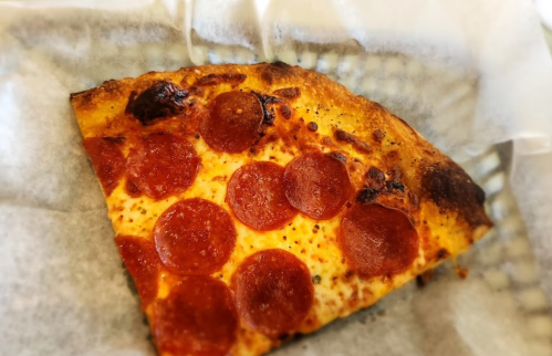 A slice of pepperoni pizza on a white paper napkin, showcasing melted cheese and crispy crust.